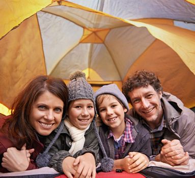Family camping is family bonding. Portrait of smiling family of four relaxing in tent on a camping holiday
