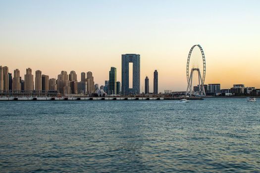 View of A Jumeirah Beach Residence and Blue waters during sunset hour. Shot made from Palm Jumeirah, man made island. Tallest ferris wheel, Ain Dubai can also be seen in the scene Dubai, UAE. Outdoors.