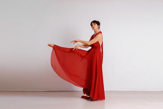 Dancer in a red flying dress. Woman ballerina dancing on a white studio background.