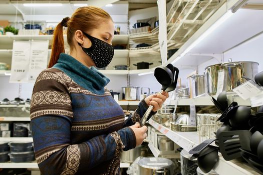 a woman in a protective mask chooses dishes and kitchen accessories in a supermarket, life with protection from infection in the new realities.
