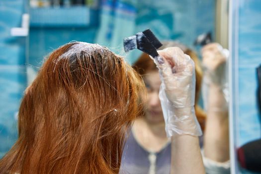 a woman dyes her hair red, coloring the hair roots with henna or dye.