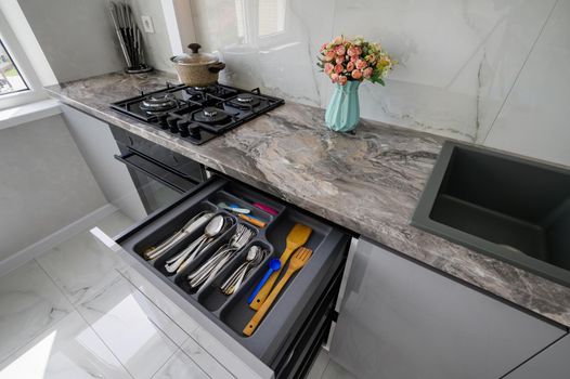 High angle closeup view to retracted drawer of grey and white modern domestic kitchen with kitchen utensils such as forks, spoons, knives