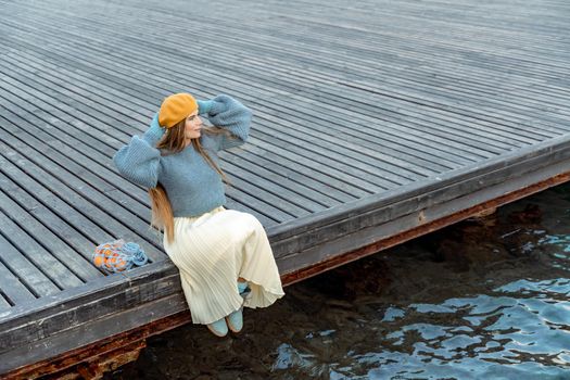 Outdoors fashion portrait of a beautiful middle aged woman walking on the beach. Marine background. Dressed in a stylish warm blue sweater, yellow skirt and beret