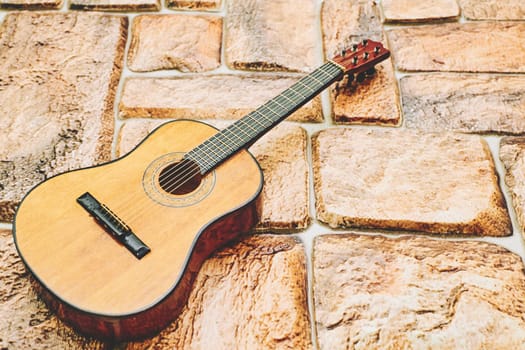 a stringed musical instrument, with a fretted fingerboard. Acoustic yellow brown guitar on orange brick cobblestone surface.