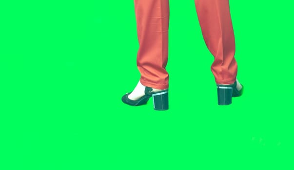 each of the limbs on which a person or animal walks and stands. Female legs in red trousers and black sandals shoes on a matte green background