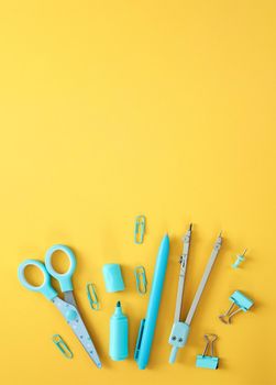 Blue stationery items on the yellow background with free space for text. Creative, colorful background with school supplies. Flatlay with copy space, top view. Marker, pen, paper clips, scissors