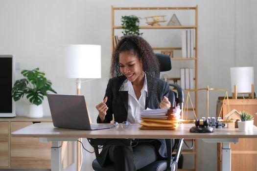 Young success american businesswoman raising her hands up and laughing with happiness at office.