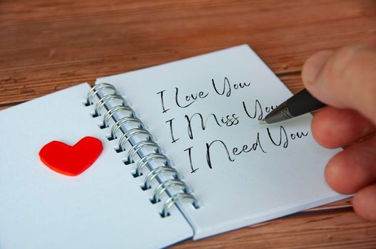 I love, miss and need you text written on white notepad. Romance and relationship concept.