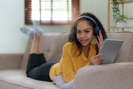 Attractive smiling young woman using tablet and listen music on sofa at home. lifestyle concept.