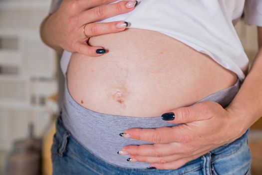 Belly of pregnant woman. A pregnant woman cannot close her jeans. The concept of clothing becomes small due to the growth of the abdomen