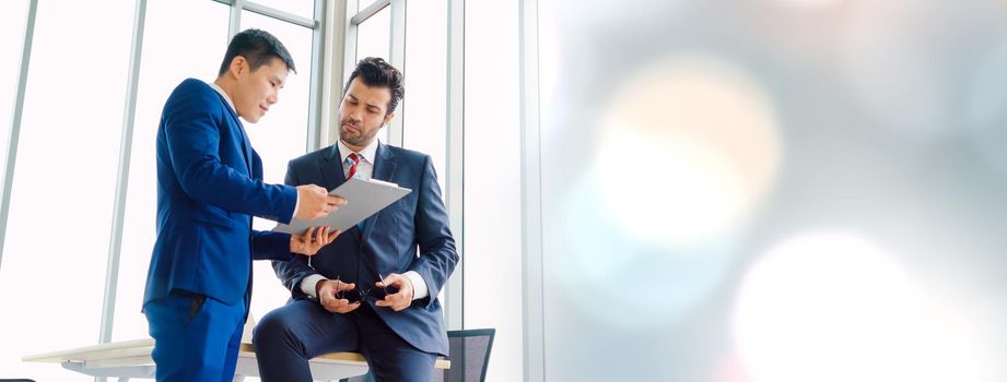 Two business people talk project strategy at office in widen view meeting room. Businessman discuss project planning with colleague at modern workplace .