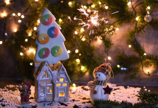 Christmas party in the toy village, a house with light in the windows and a marshmallow tree, sparkler and bokeh from a garland. High quality photo