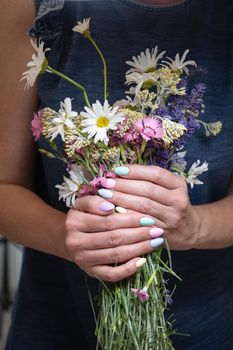 a young woman with a beautiful summer manicure holds a bouquet of wild flowers in pastel shades. High quality photo