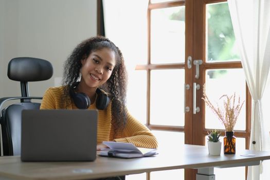 Smiling young African American woman in headphones distracted from computer work look in distance dreaming. Happy biracial female study online at home on laptop thinking or planning. Vision concept..