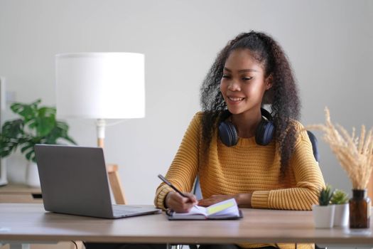 Young adult happy smiling Hispanic Asian student wearing headphones talking on online chat meeting using laptop in university campus or at virtual office. College female student learning remotely..