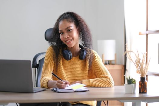 Smiling young African American woman in headphones distracted from computer work look in distance dreaming. Happy biracial female study online at home on laptop thinking or planning. Vision concept..