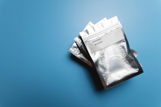 transparent plastic aligners lie in a zip bag with a label under your name, close-up, on a blue background.