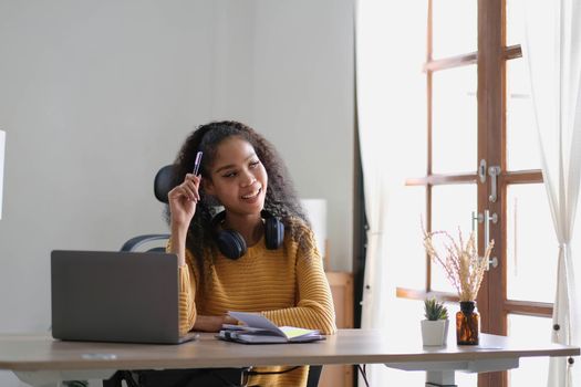 Young adult happy smiling Hispanic Asian student wearing headphones talking on online chat meeting using laptop in university campus or at virtual office. College female student learning remotely..