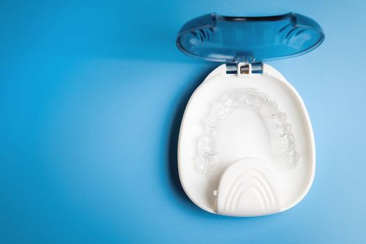 orthodontic care, new invisible plastic aligners printed on a 3d printer lie in a special white box, on a blue background without people.