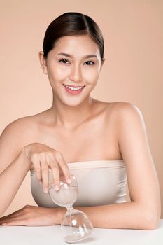 The concept of anti-aging demonstrated by closeup portrait of an ardent young woman holding an hourglass. Skincare treatment, beauty care and cosmetic ideas.