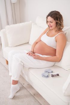 Pregnant woman sits on a white sofa and holds a smartphone. Fetal ultrasonic screening