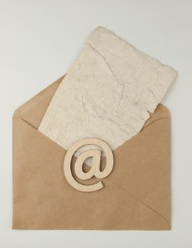 An e-mail sign on a brown envelope with blank crumpled old paper sheet lies on a white background. Concept e-mail message letter. Top view