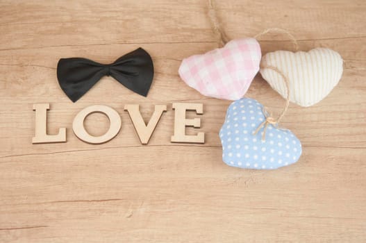 word Love from wooden letters with colorful fabric hearts on a wood background. Happy Valentines Day