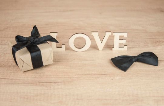 wooden word LOVE with butterfly tie and gift box on wood table. Happy Valentines Day