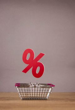 Shopping cart from the supermarket with sign percent over gray paper wall background. Shopping in the Mall, shop, shopping, a large selection.