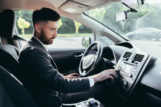 Businessman driving a car turns on the music in the car player, a man before a trip in a business suit