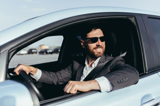 Businessman in black glasses sitting behind the wheel of a car