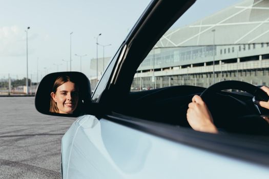 The woman is sitting in the car, beating in the side mirror, successful and joyful