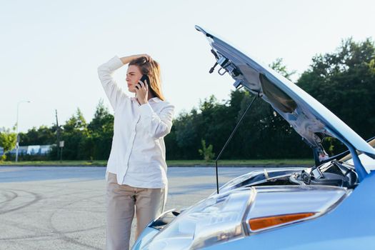 An annoyed and angry woman, near a broken car, tries to call an insurance agent and a repair crew. for car repair