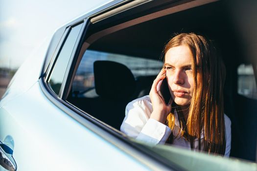 Beautiful female car passenger looks out the window and talks on the phone, close-up photo