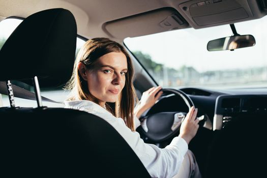 Portrait of a successful woman driving a car, smiling rejoicing and looking at the camera