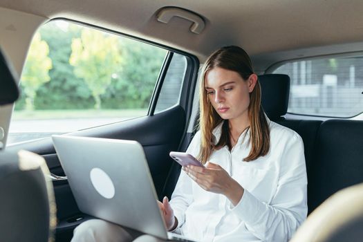 Beautiful female passenger car works on a laptop and uses a mobile phone
