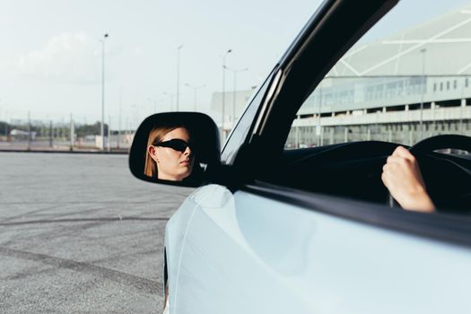 The woman is sitting in the car, beating in the side mirror, successful and joyful