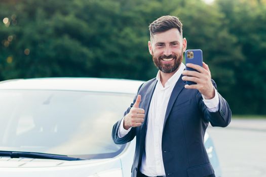 A cheerful man is talking on a video call near his new car