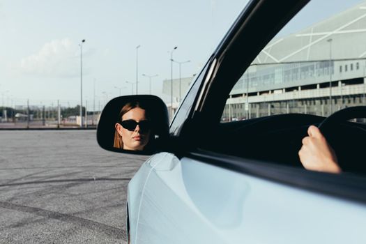 The woman is sitting in the car, beating in the side mirror, successful and joyful