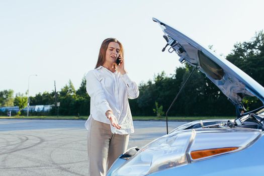 An annoyed and angry woman, near a broken car, tries to call an insurance agent and a repair crew. for car repair