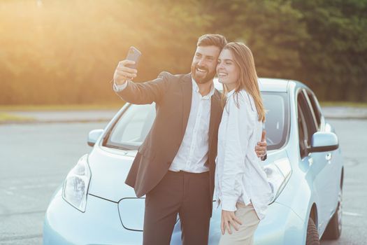 Young beautiful couple man and woman, happy to buy a new car, take photos together on the phone, and show friends shopping by video call