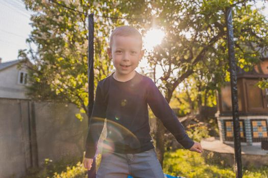 little boy jumps on a trampoline that stands in the yard