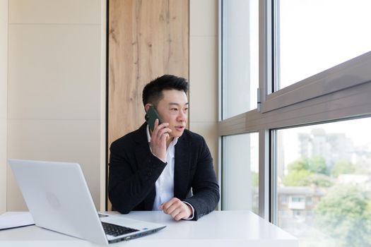 Serious asian business businessman uses cellphone to communicate with colleagues while sitting in modern office