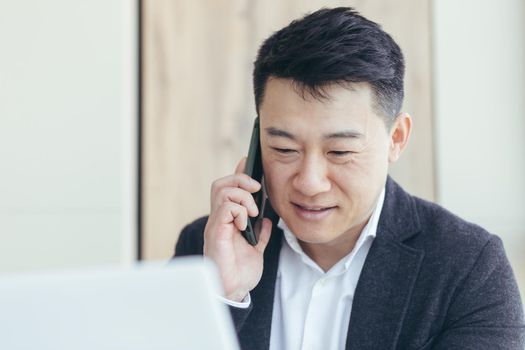 Asian businessman close-up portrait, successful and happy smiling talking on the phone, in a business suit