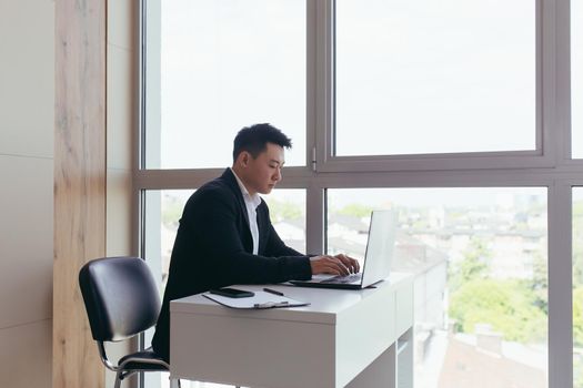 Asian businessman working on laptop sitting in modern office