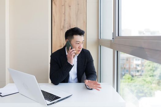 Serious asian business businessman uses cellphone to communicate with colleagues while sitting in modern office