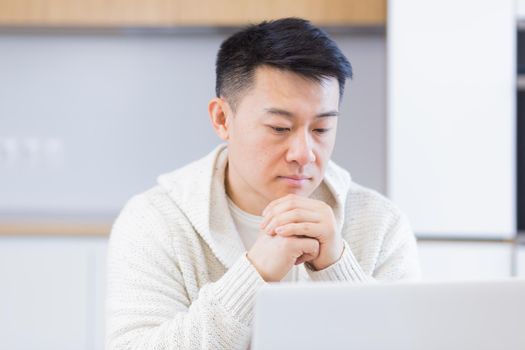 Thoughtful serious young asian man looking away. student writer sit at home office desk with laptop thinking of inspiration search solution ideas lost in thoughts dreaming solving financial problems