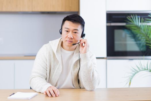 Asian man talking online on video call at home room with headset. Male in casual clothes looking at camera, meeting or conference in distance. Portrait student or teacher Lecture training. Webcam view