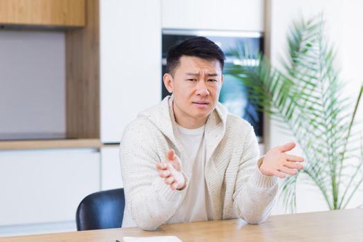 Asian man talking online on video call at home in living room or kitchen. male in casual clothes looking at camera, meeting or conference in distance. Portrait teacher. Lecture training. Webcam view