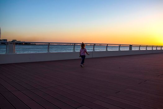 Little girl running on the boardwalk during sunset hour. Outdoors.